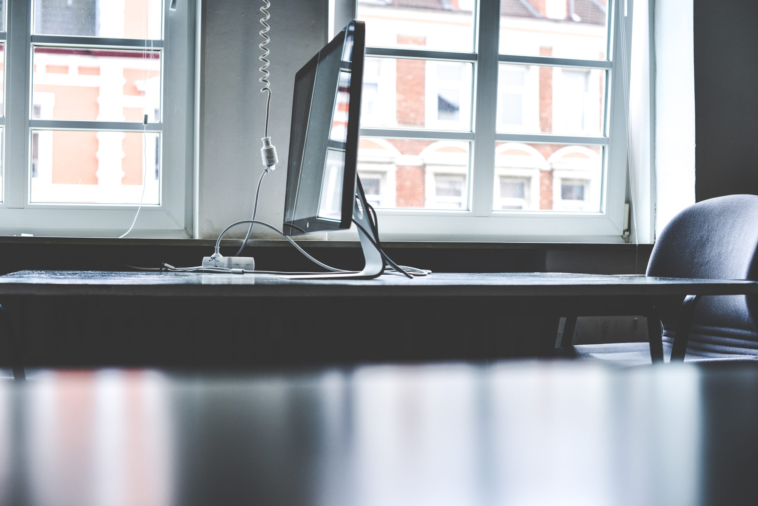 Photo of a Mac monitor on a desk in front of some Windows