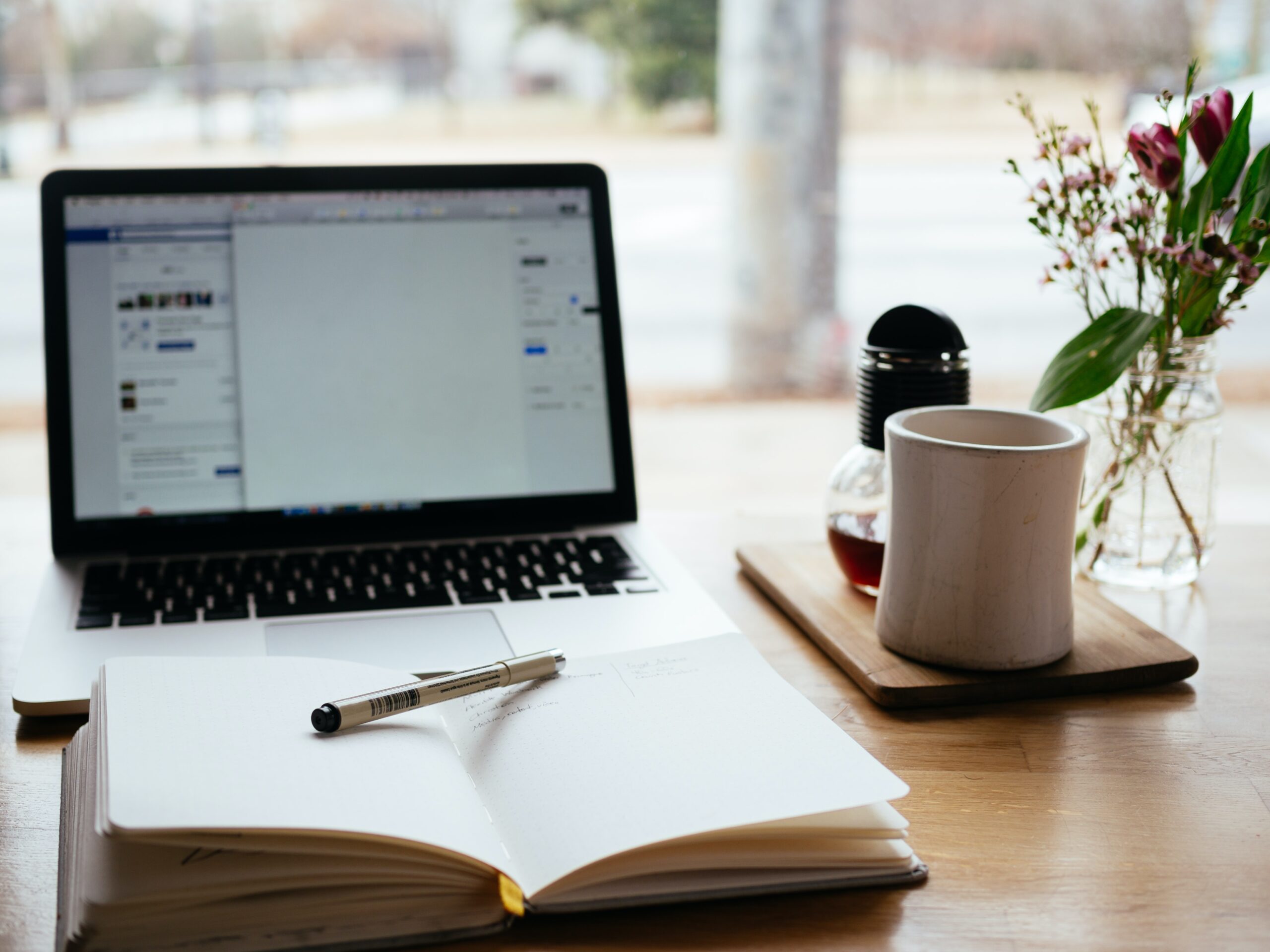 Photo of a laptop on a desk with a notebook and a coffee